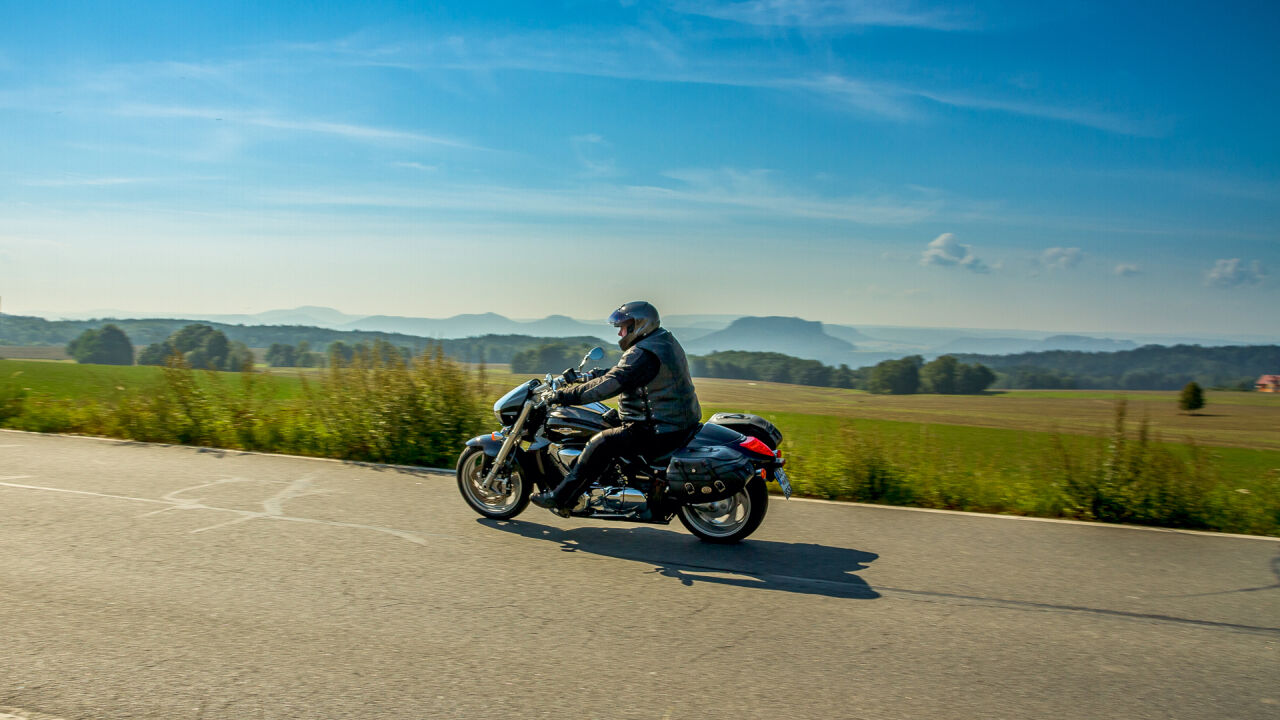 Motorradfahrer auf einer Landstraße, dahinter flache Felder und am Horizont Tafelberge Motorradfahrer auf einer Landstraße, dahinter flache Felder und am Horizont Tafelberge