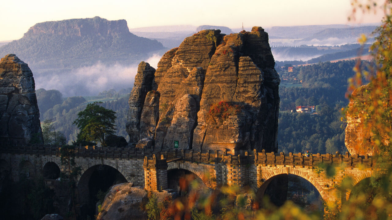 Steinerne Bogenbrücke zwischen hohen Sandsteinfelsen, dahinter ein Tafelberg im Morgenlicht Steinerne Bogenbrücke zwischen hohen Sandsteinfelsen, dahinter ein Tafelberg im Morgenlicht